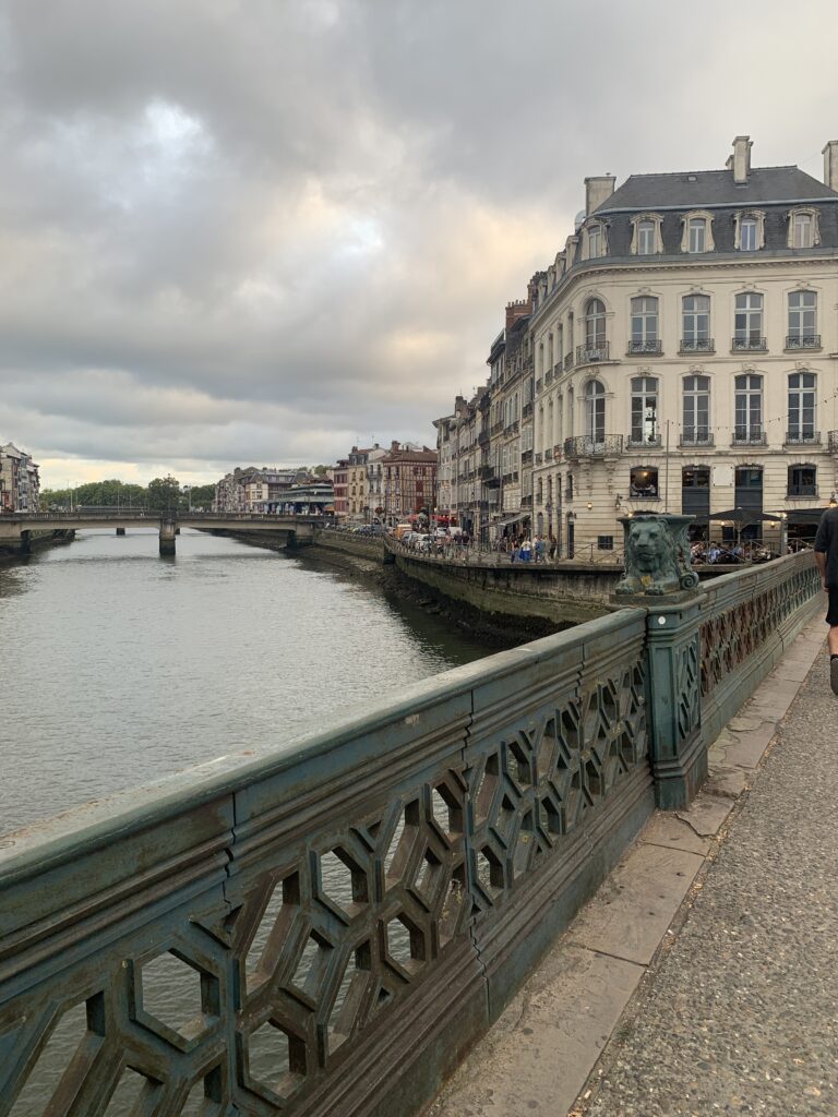 quais nive bayonne en famille Road trip au Portugal en famille : 8 jours entre Lisbonne, Batalha et Nazaré avec nos enfants Vue d'une passerelle en métal surplombant une rivière, avec des bâtiments historiques sur les rives et un ciel nuageux au crépuscule.